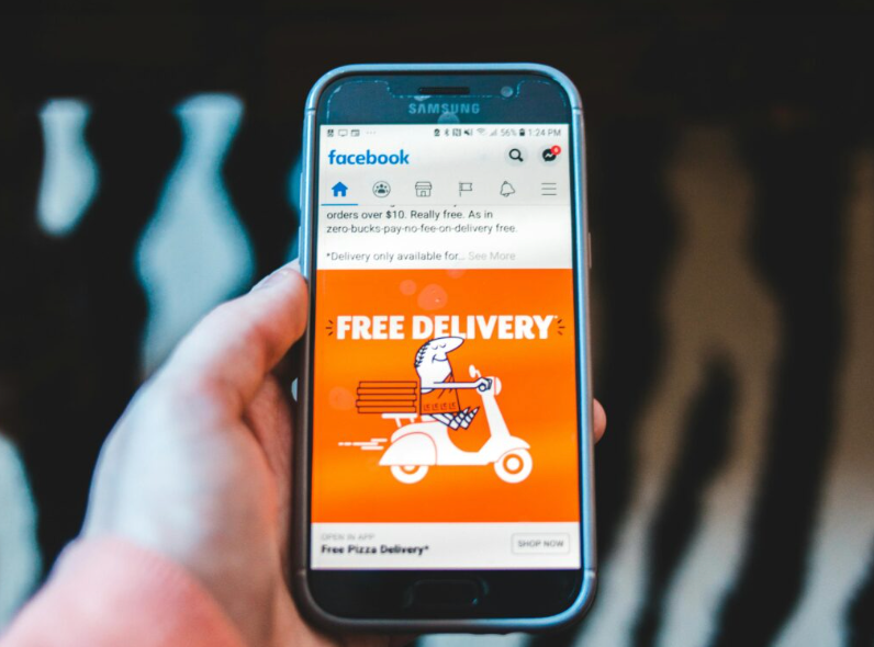 Hand holding a smartphone showing a Facebook food delivery ad on screen.